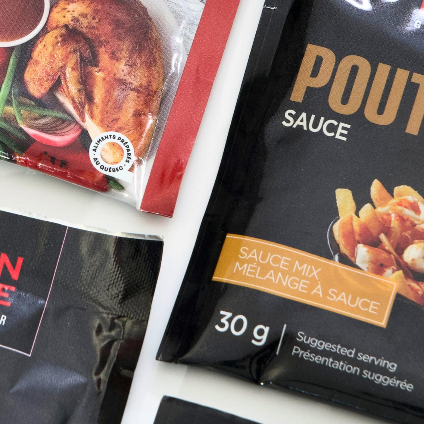 Image de différents emballages de mélanges de sauces, y compris une sauce pour poutine et un assaisonnement pour poulet, avec le label 'Aliments préparés au Québec