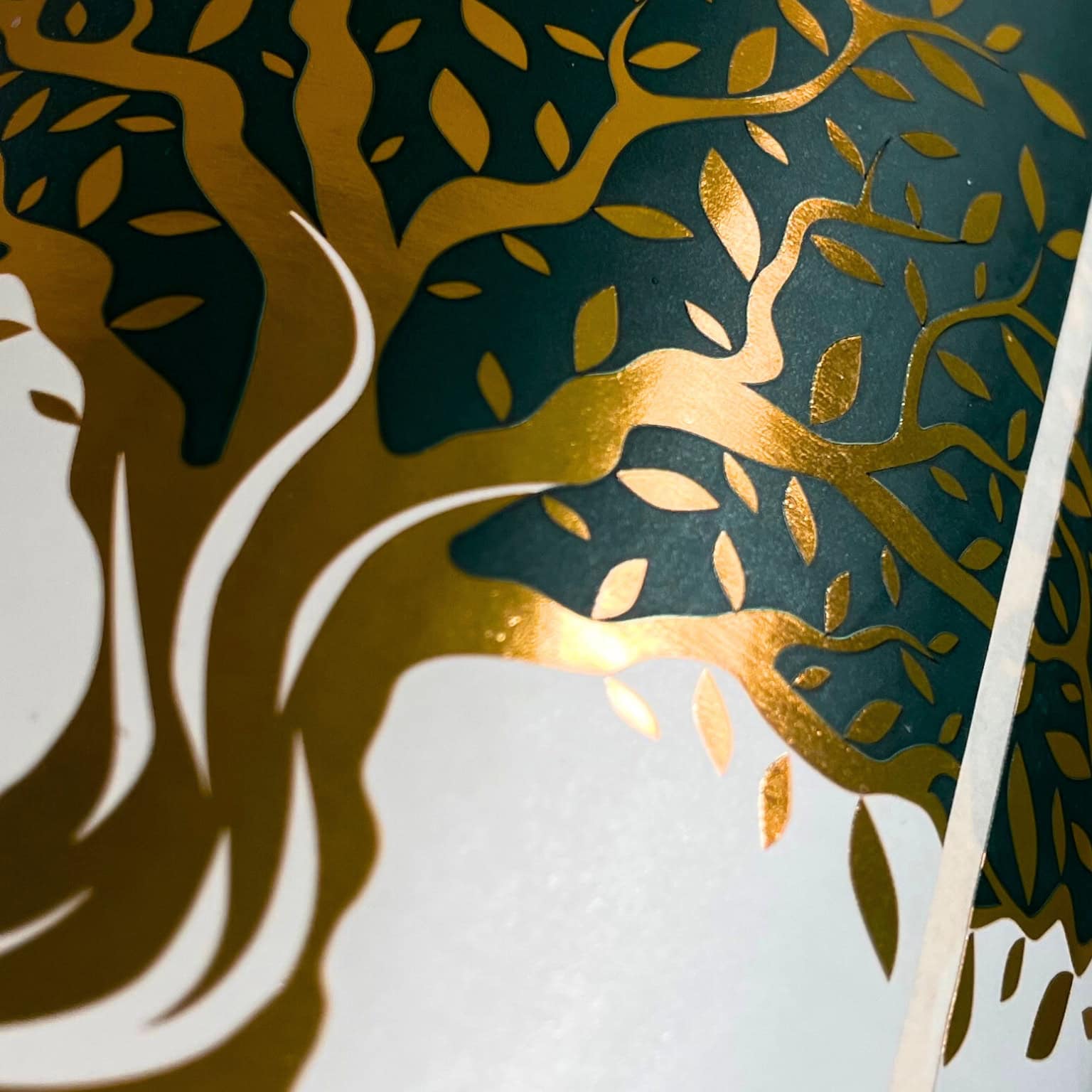 Gros plan d’un design en doré et vert représentant un arbre sur un emballage pour illustrer la technique de finition d’estampage à froid.