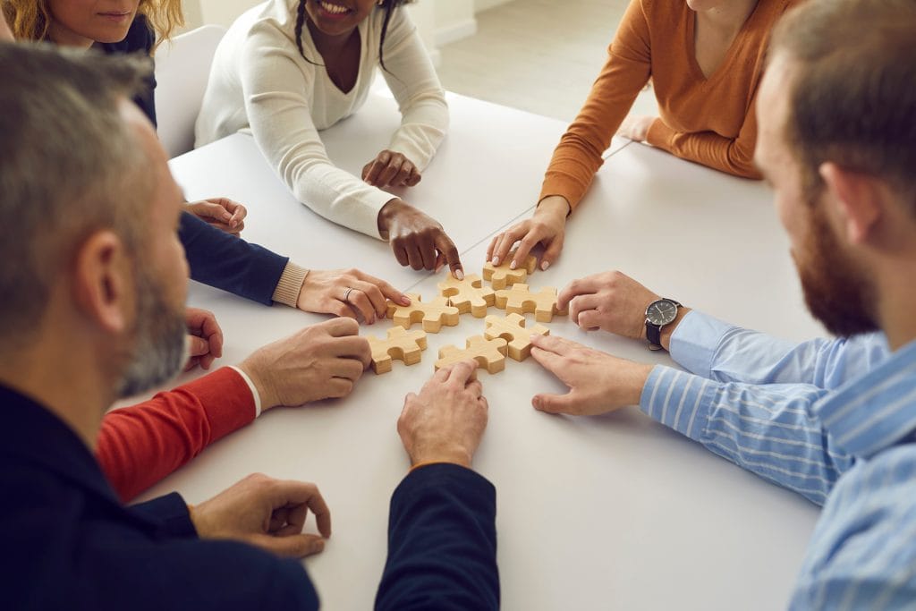 Image d'un groupe de personnes travaillant ensemble pour assembler des pièces de puzzle en bois sur une table.