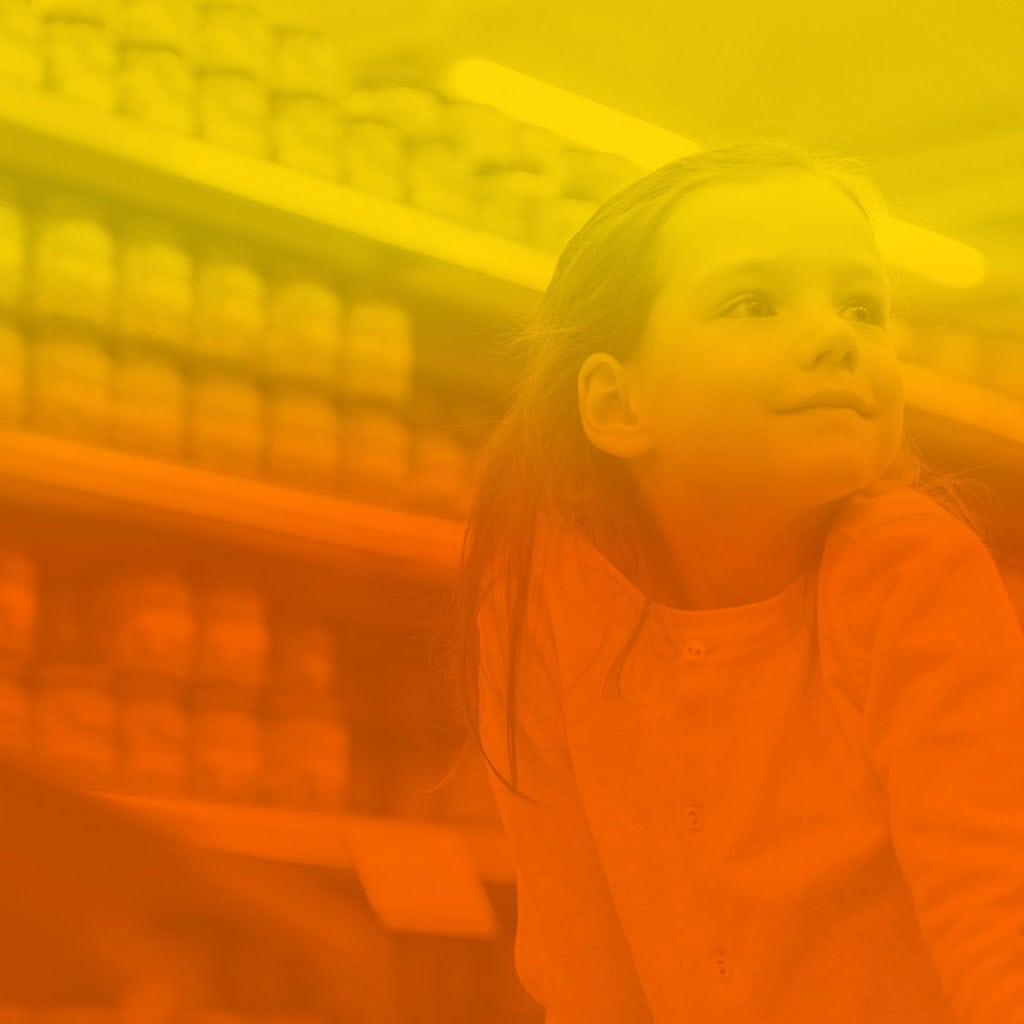 Jeune fille souriante dans une allée de magasin avec des étagères remplies de produits en arrière-plan, avec un filtre jaune et rouge sur l'image.