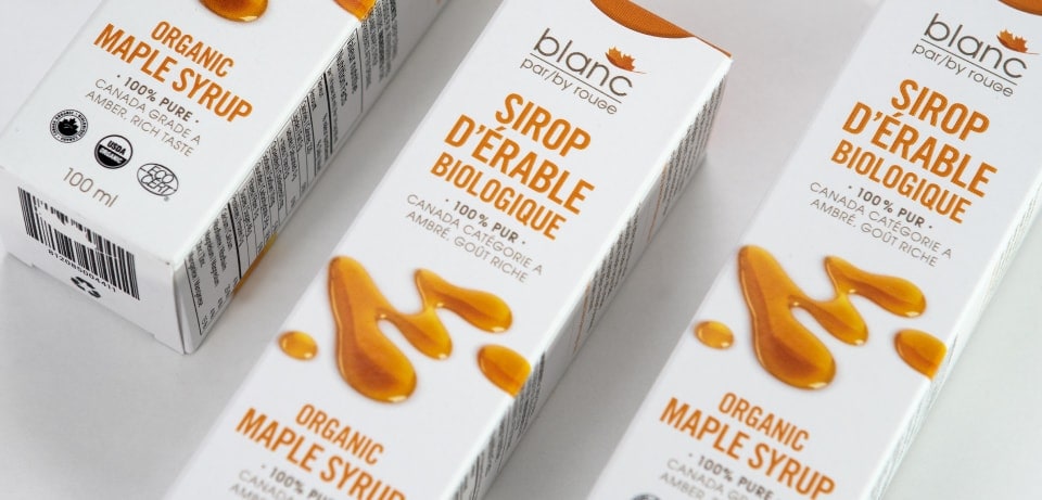 Emballages de Sirop d’Érable Biologique Blanc par Rouge Image de plusieurs emballages de sirop d'érable biologique de la marque Blanc par Rouge, avec des illustrations de sirop versé sur les boîtes.