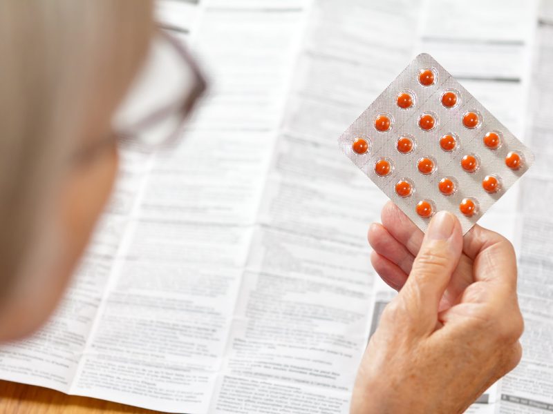 Image d'une personne âgée tenant une plaquette de comprimés et lisant la notice du médicament.
